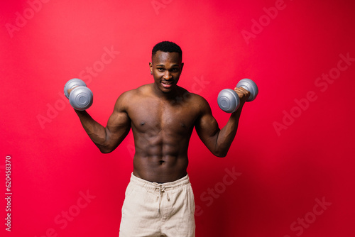 Powerful man doing the exercises with dumbbells on red background. Strength and motivation