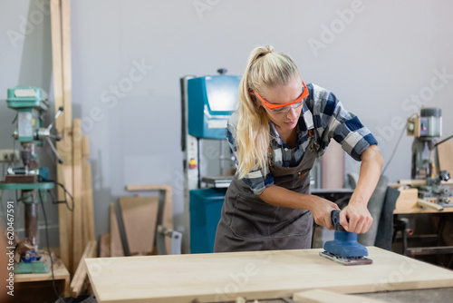 Quadro su tela young carpenter caucasian woman using electric wood sander on wood at manufacturing wooden industry