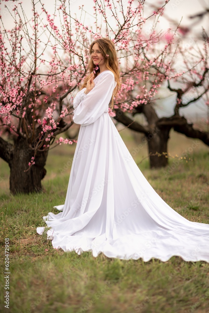 Woman peach blossom. Happy curly woman in white dress walking in the garden of blossoming peach trees in spring Woman peach blossom. Happy curly woman in white dress walking in the garden of blossoming peach trees in spring