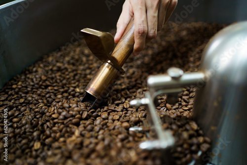 Professional coffee roaster working with modern automated roasting machine in the coffee roasting factory. Food and beverage business concept.
