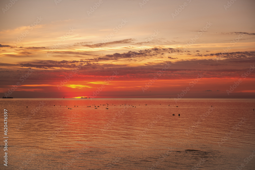 Silhouette of people on SUP boards on the horizon of the sea at orange sunrise. Active hobby on the water. balance state. mental health. Leisure activities while traveling. Sea landscape. Copy space