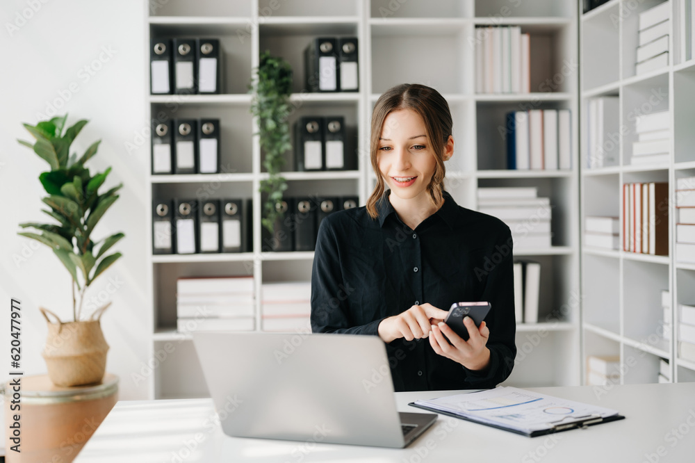 Confident business expert attractive smiling young woman typing laptop ang holding digital tablet on desk in office.. Confident business expert attractive smiling young woman typing laptop ang holding digital tablet on desk in office..