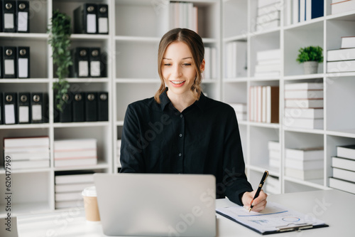 Confident business expert attractive smiling young woman typing laptop ang holding digital tablet on desk in office.. © Nuttapong punna