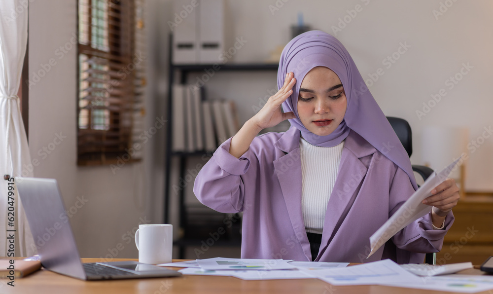 A stressed Asian business asian islamic woman in hijab holding documents is working from home, feeling stressed because of lot of paperwork appearing worried, tired, and overwhelmed A stressed Asian business asian islamic woman in hijab holding documents is working from home, feeling stressed because of lot of paperwork appearing worried, tired, and overwhelmed