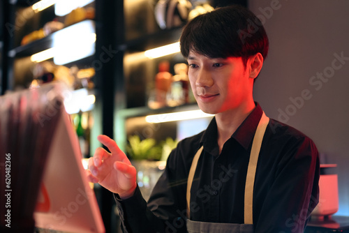 Handsome male waiter touching display of electronic cash register, entering customer order at bar or coffee shop