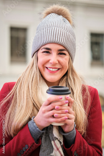 Portrait of young caucasian blonde woman with a coffee cup on the street in winter.