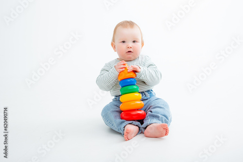 charming baby in a T-shirt and jeans is playing with toy pyramid, a postcard, a banner, a place for text. High quality photo © Olesya Pogosskaya