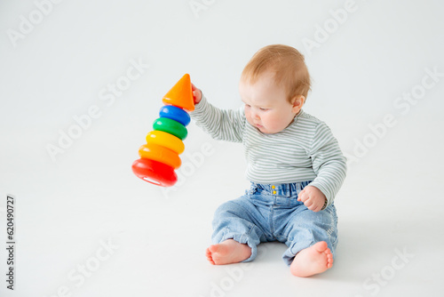 charming baby in a T-shirt and jeans is playing with toy pyramid, a postcard, a banner, a place for text. High quality photo