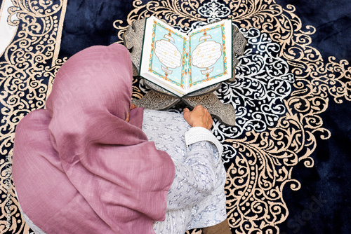 top view of woman sitting in the mosque and reading muslim book arabic calligraphy Quran translation : holy book and verses text fatiha mean open and bakara mean the cow  and on a wooden stand photo