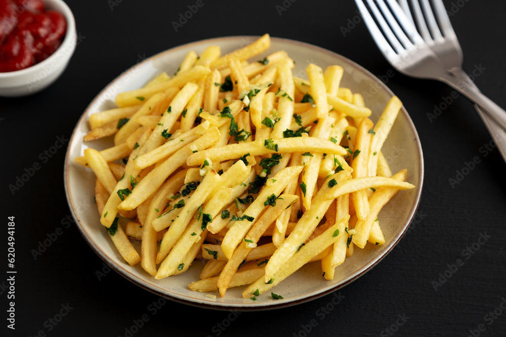 Garlic French Fries with Parsley on a Plate on a black background, side view. Garlic French Fries with Parsley on a Plate on a black background, side view.