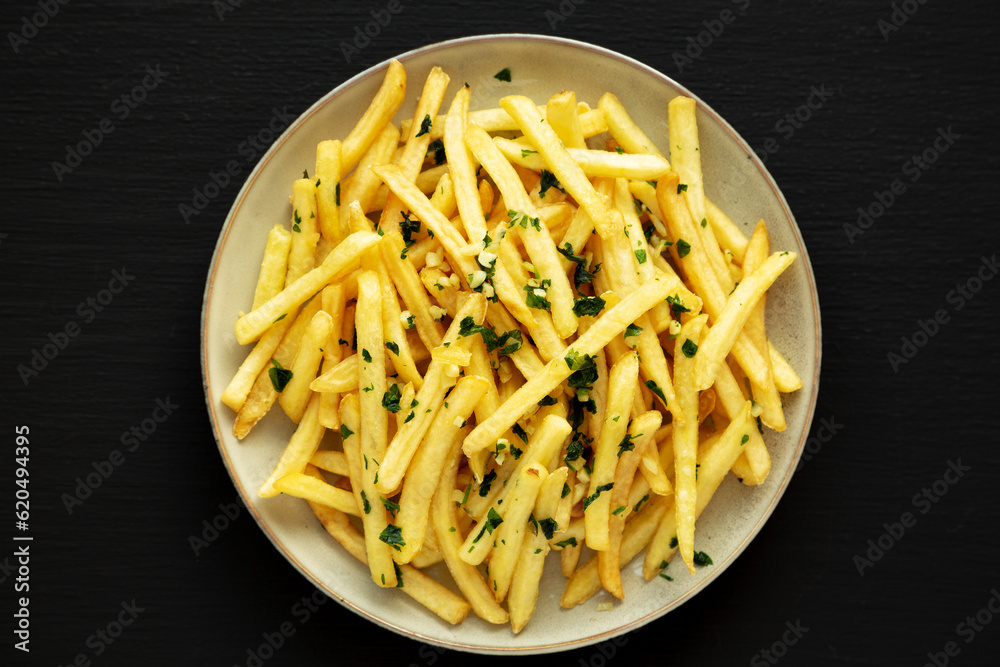 Garlic French Fries with Parsley on a Plate on a black background, top view. Overhead, from above, flat lay. Garlic French Fries with Parsley on a Plate on a black background, top view. Overhead, from above, flat lay.