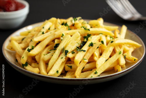 Garlic French Fries with Parsley on a Plate on a black background, side view. Close-up.