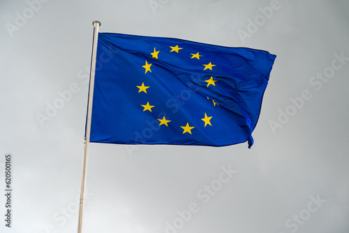 EU flag waving in the wind against dark cloudy sky. Flag of European Union flying on a pole. 