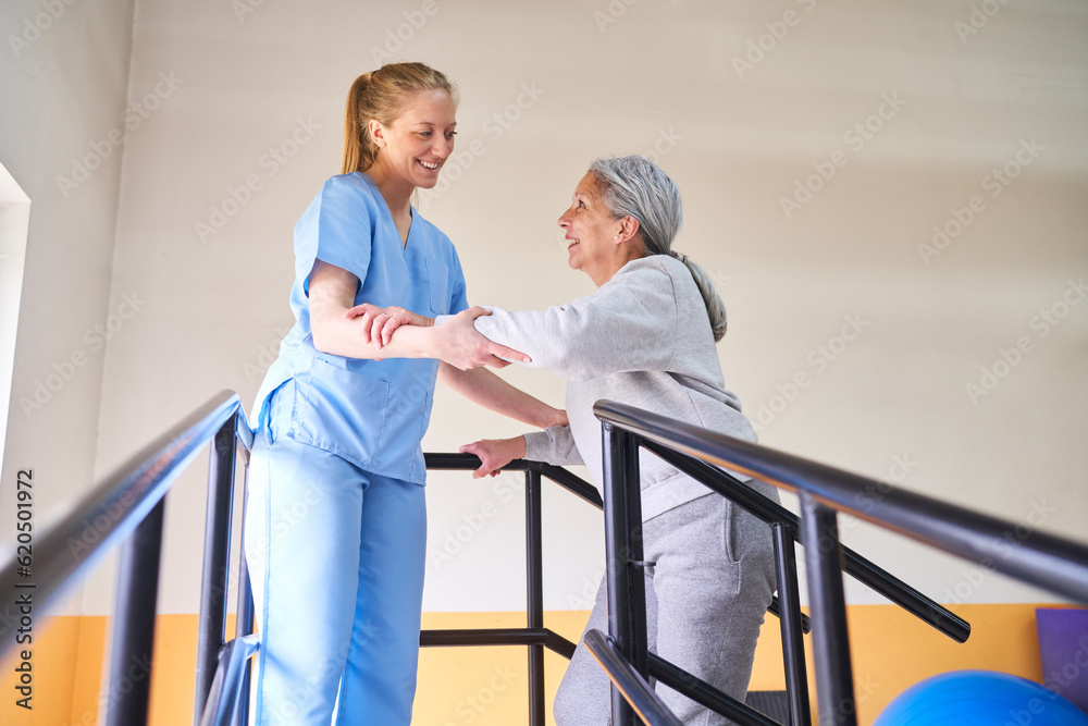 Obraz premium Young physiotherapist assisting elderly woman in movement therapy