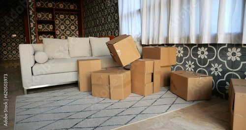 Scattered cardboard boxes in living room create messy pile. In slow motion, empty box flies in and joins jumble of boxes. Scene portrays remnants of child's play, with hint of required cleaning