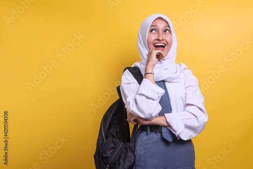 Happy Indonesian high school female muslim student in white and grey uniform looking up at copy space photo