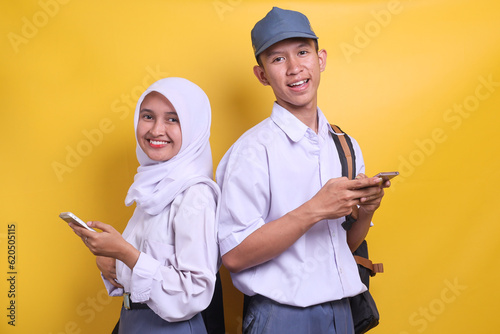 Two Indonesian senior high school student wearing white and grey uniform smiling while holding a mobile phone and books photo