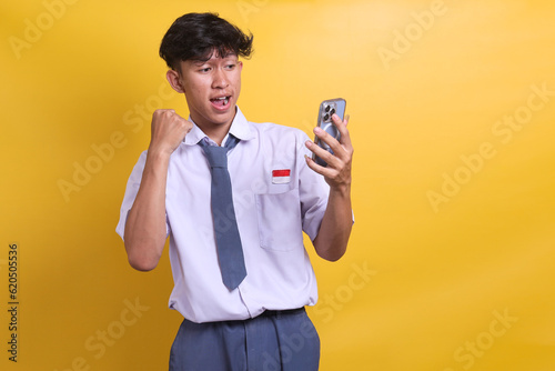 Indonesian senior high school student wearing white and grey uniform holding cell phone celebrating great result with yes gesture photo