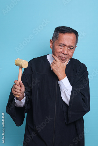Judge Asian man thinking while holding gavel hammer isolated on blue background 