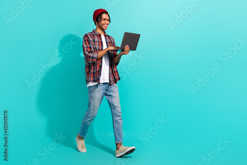 Full length profile portrait of nice positive man use wireless netbook walking empty space isolated on turquoise color background