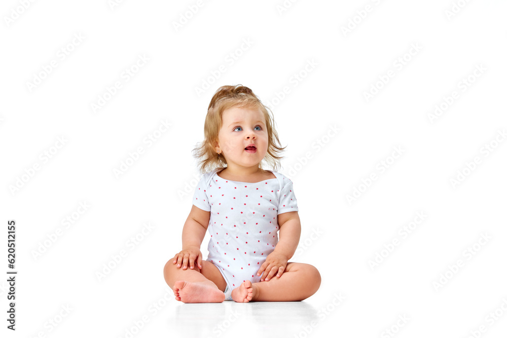 Curious child. Little, cute baby girl, toddler in diaper sitting on floor and attentively looking against white studio background Curious child. Little, cute baby girl, toddler in diaper sitting on floor and attentively looking against white studio background