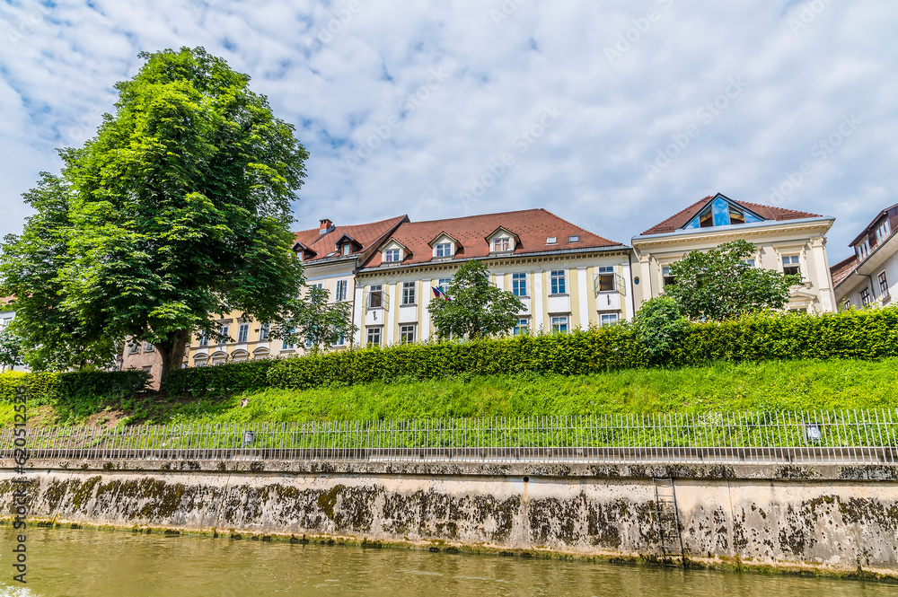 A view of building beside the Ljubljanica River approaching the Saint James Bridge in Ljubljana, Slovenia in summertime