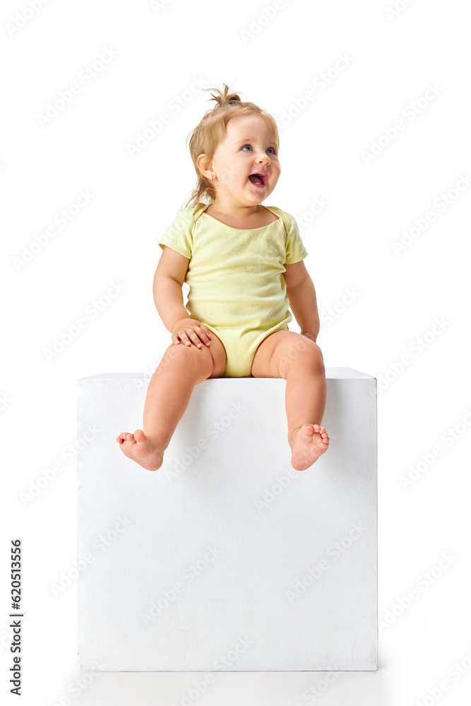 Portrait of beautiful little girl, toddler in yellow clothes sitting and cheerfully laughing against white studio background Portrait of beautiful little girl, toddler in yellow clothes sitting and cheerfully laughing against white studio background