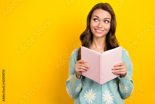 Photo of young cheerful positive smiling hold copybook enjoy reading literature look empty space plans for future isolated on yellow color background