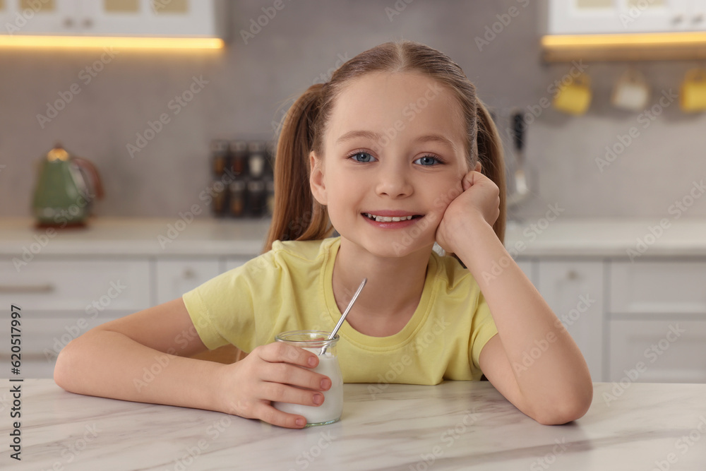 Cute little girl with tasty yogurt at white marble table in kitchen Cute little girl with tasty yogurt at white marble table in kitchen