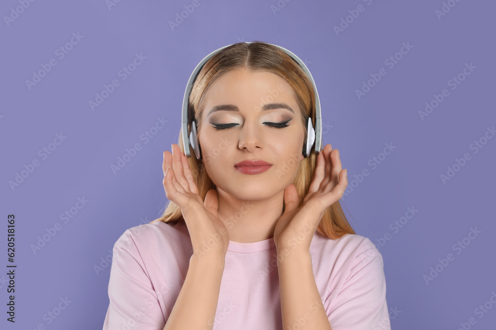 Beautiful woman in headphones enjoying music on violet background Beautiful woman in headphones enjoying music on violet background