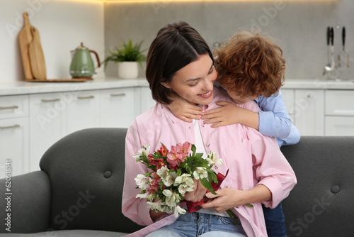 Little son congratulating his mom with Mother`s day at home. Woman holding bouquet of flowers