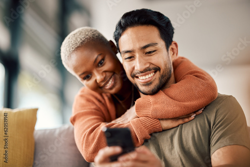 Phone, interracial couple and technology on a sofa at home reading text in a living room. Support, young people and hug together in a house sitting on a lounge couch with mobile streaming and video