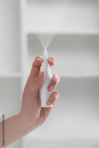 Woman using nasal spray indoors, closeup view