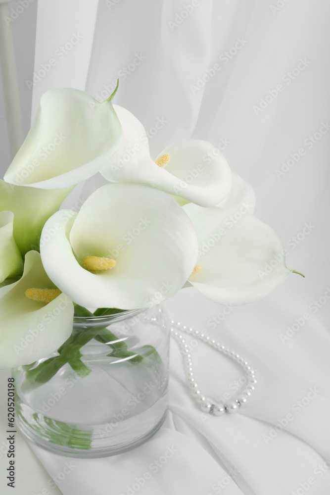 Beautiful calla lily flowers in glass vase on white cloth Beautiful calla lily flowers in glass vase on white cloth