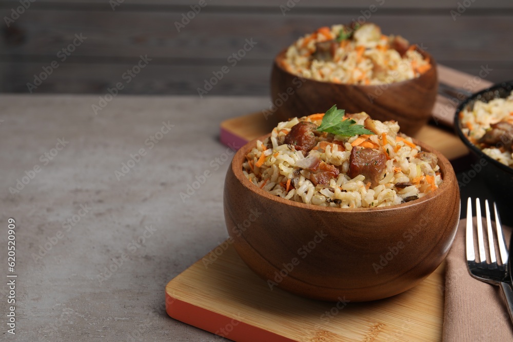 Delicious pilaf with meat and carrot in bowl on grey textured table. Space for text Delicious pilaf with meat and carrot in bowl on grey textured table. Space for text