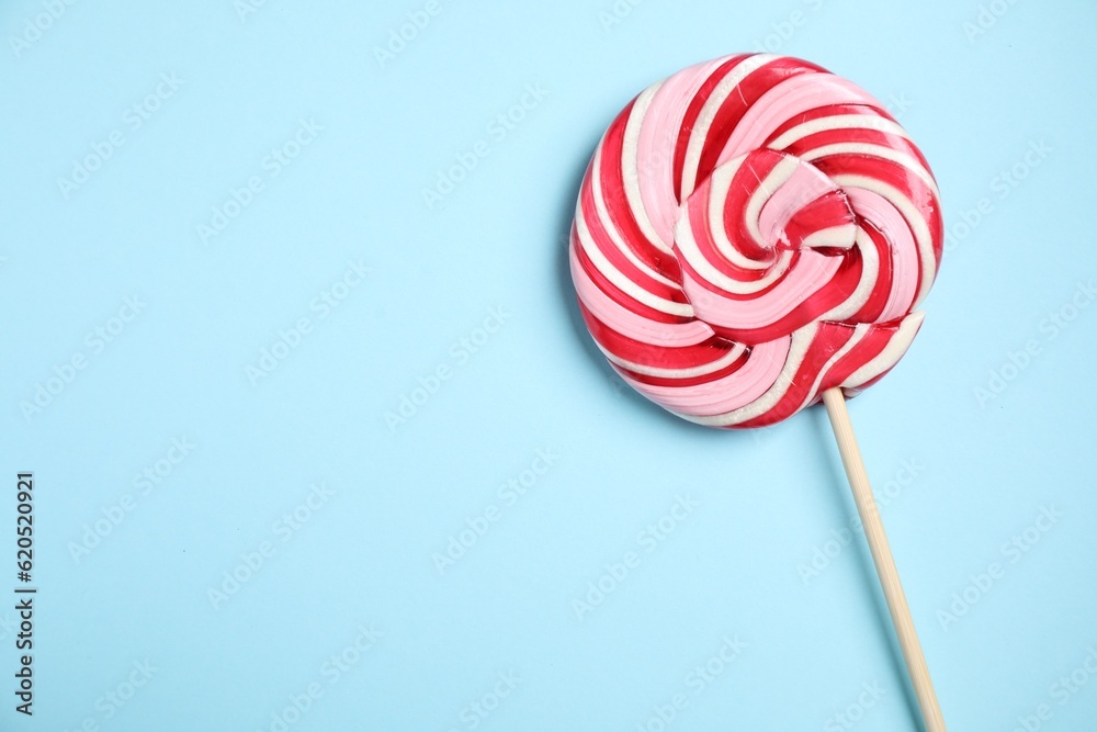 Stick with colorful lollipop swirl on light blue background, top view. Space for text