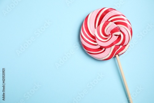Stick with colorful lollipop swirl on light blue background, top view. Space for text