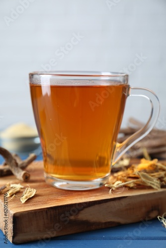 Aromatic licorice tea in cup and dried sticks of licorice root on blue wooden table, closeup