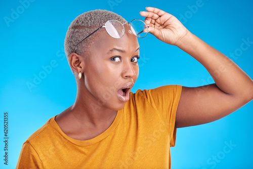 Portrait, news and black woman shocked, gossip and announcement against a blue studio background. Face, female person and model with glasses, surprise and deal with omg facial and wow with expression