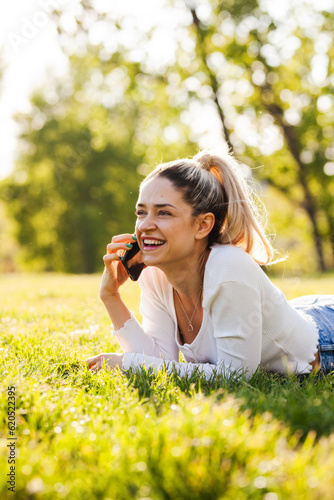 Beautiful girl lying in a field in the park. Talking on phone.