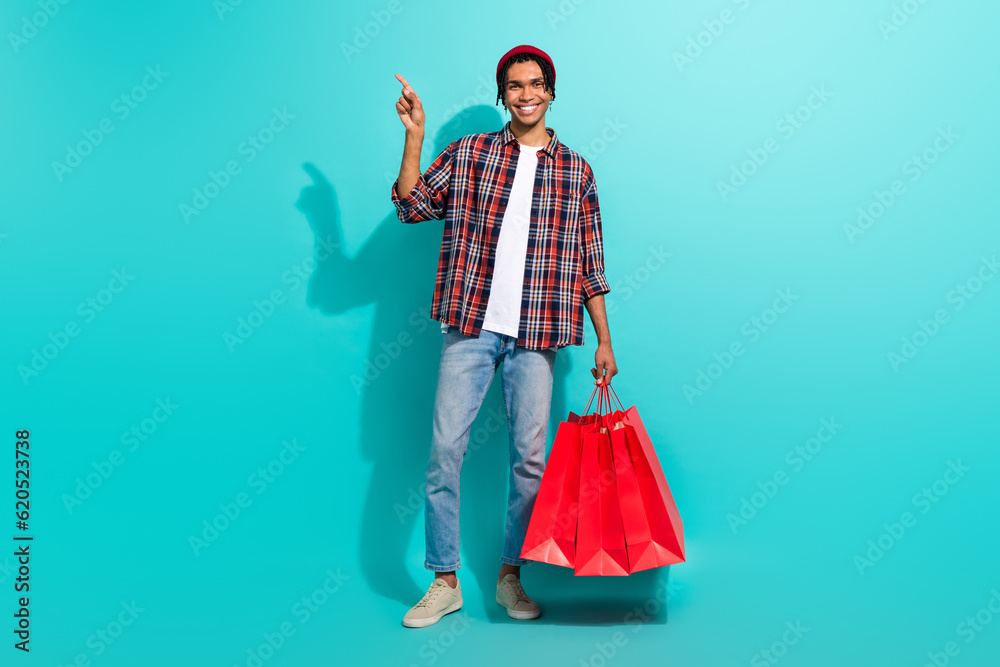 Full body portrait of cheerful man hold store mall bags indicate finger empty space offer isolated on turquoise color background