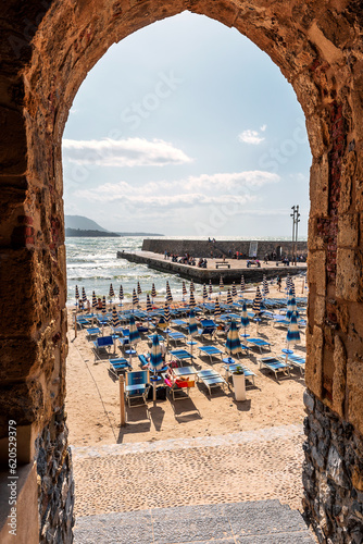 Archway through an ancient stone building leading to a beach with unrecognizable people in Cefalu, Sicily, Italy