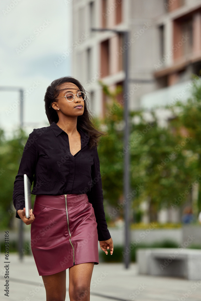 Portrait of beautiful young african gir, office worker walking along the street to work. Concentrated and motivated employee Portrait of beautiful young african gir, office worker walking along the street to work. Concentrated and motivated employee