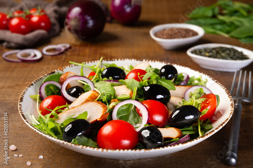 Salad with grilled chicken fillet meat, fresh vegetables, spinach, arugula (ruccola), red onion, cherry tomato and olives. Healthy menu. Diet food. Wooden background.