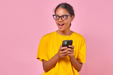 Young inspired Indian woman in casual clothes holding mobile phone and shouting loudly after reading alert in banking application about receipt of money in account stands on isolated pink background.