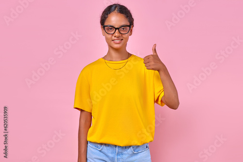 Принти на полотні Young positive casual Indian woman teenager making approving gesture positively evaluating quality of advertising product or level of services rendered stands on isolated pink background