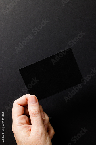 Vertical image of hand of caucasian woman with business card with copy space on black background
