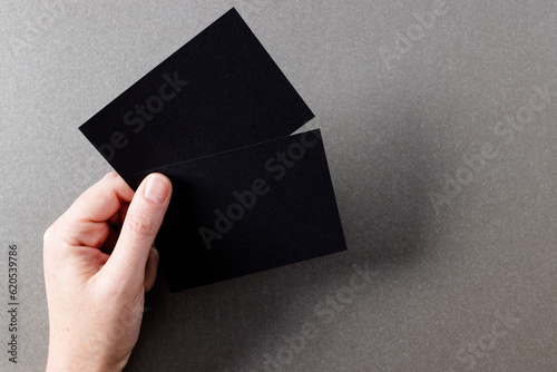 Hand of caucasian woman holding black business cards with copy space on grey background