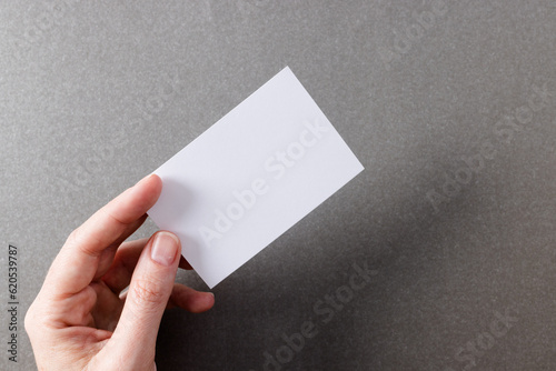 Hand of caucasian woman holding white business card with copy space on grey background