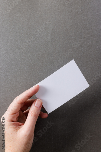 Vertical image of hand of caucasian woman with business card with copy space on grey background
